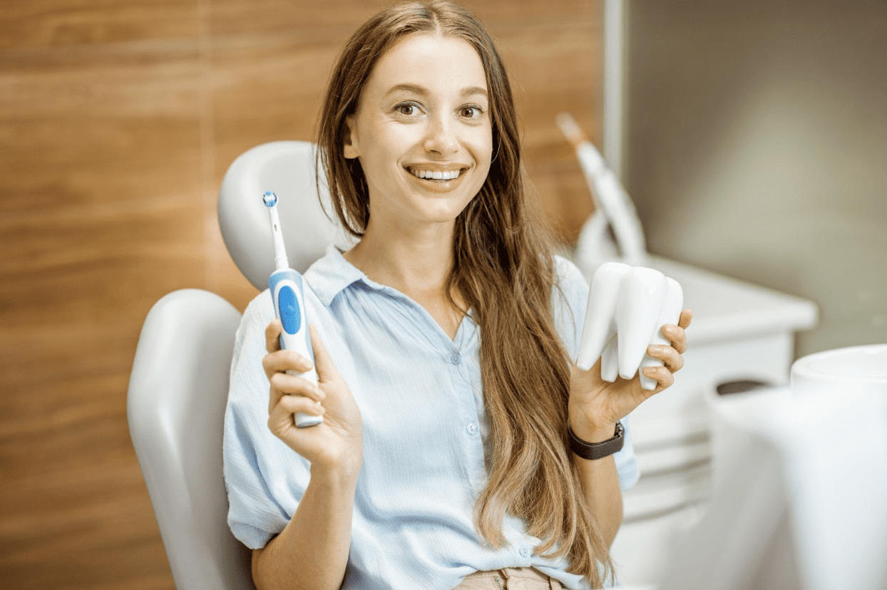 Teenage girl sitting happily, holding a model tooth in one hand and a toothbrush in the other.