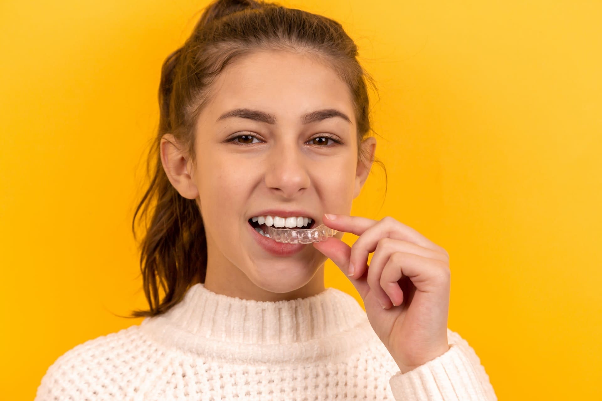 Teenage girl placing Invisalign aligners on her teeth.