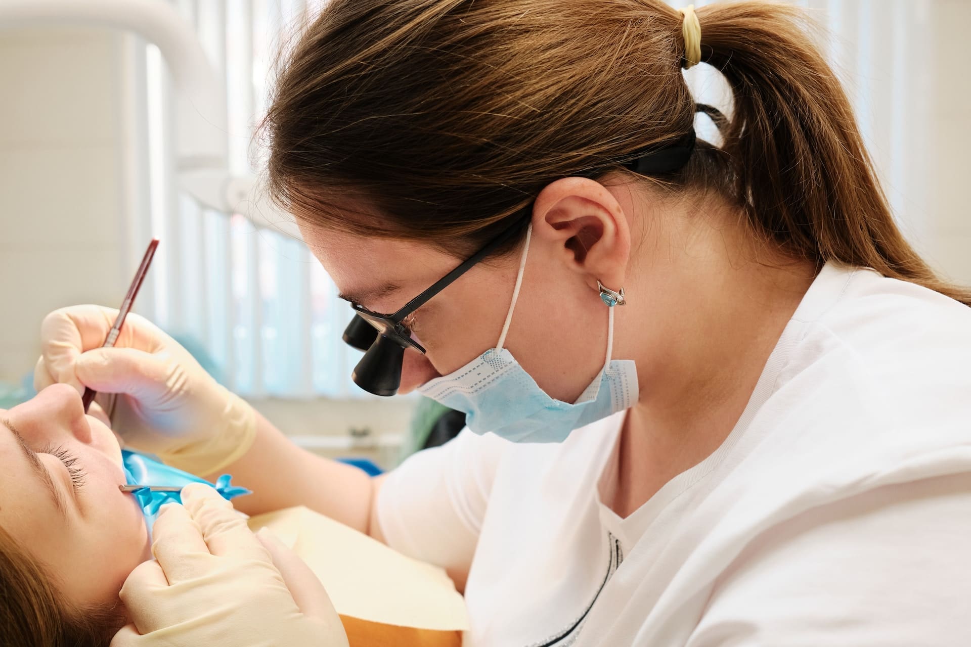Focused dentist closely examining patient's teeth with the assistance of dental microscopic glasses.