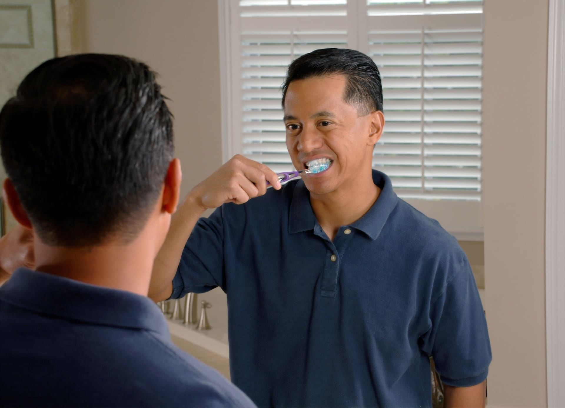 Male patient brushing his teeth and smiling while looking at himself in the mirror.