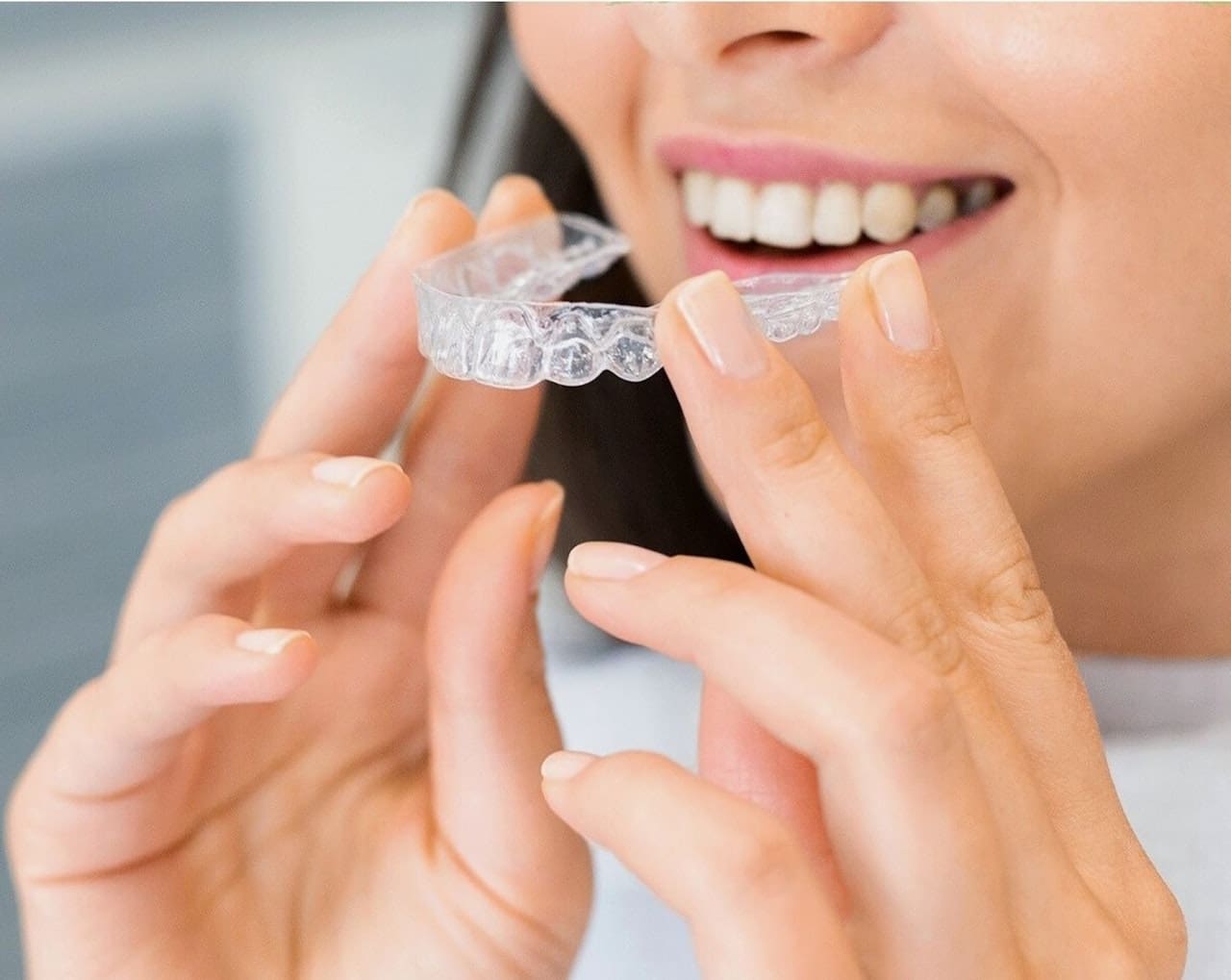 Smiling woman looking happy while applying Invisalign aligners on her teeth.