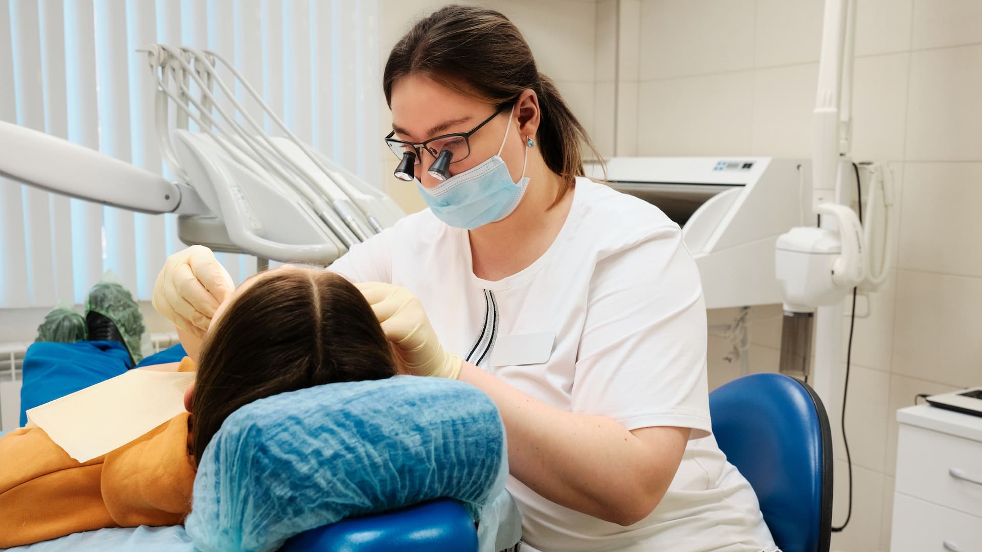 Dentist wearing glasses with attached lenses, providing dental treatment to a patient.