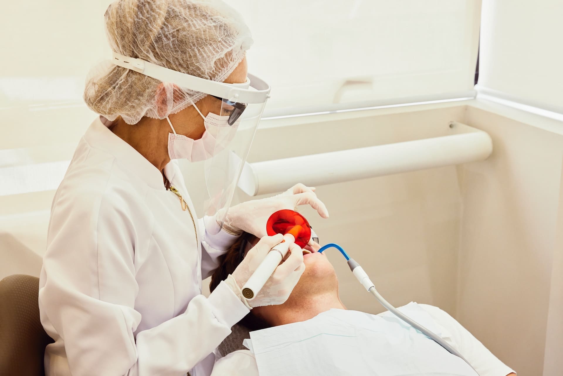 Dentist in surgical uniform, mask, and gloves providing dental treatment to the patient, handling medical instruments.
